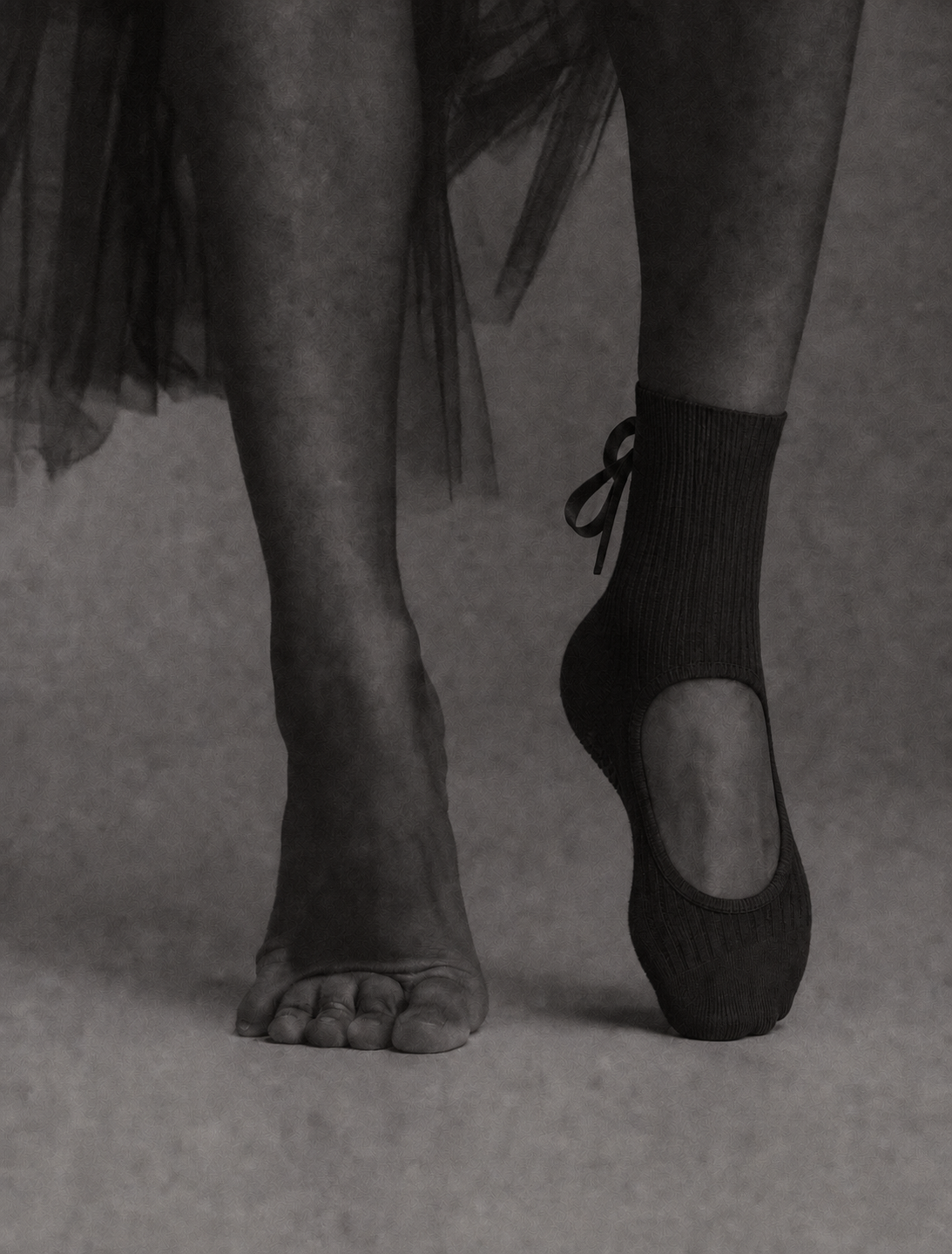 Black ballet-influenced grip sock shown beside a bare foot.